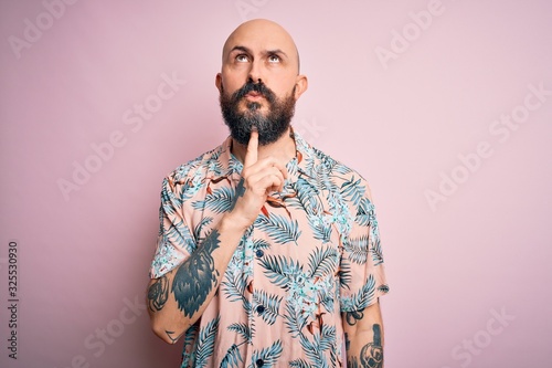 Handsome bald man with beard and tattoo wearing casual floral shirt over pink background Thinking concentrated about doubt with finger on chin and looking up wondering