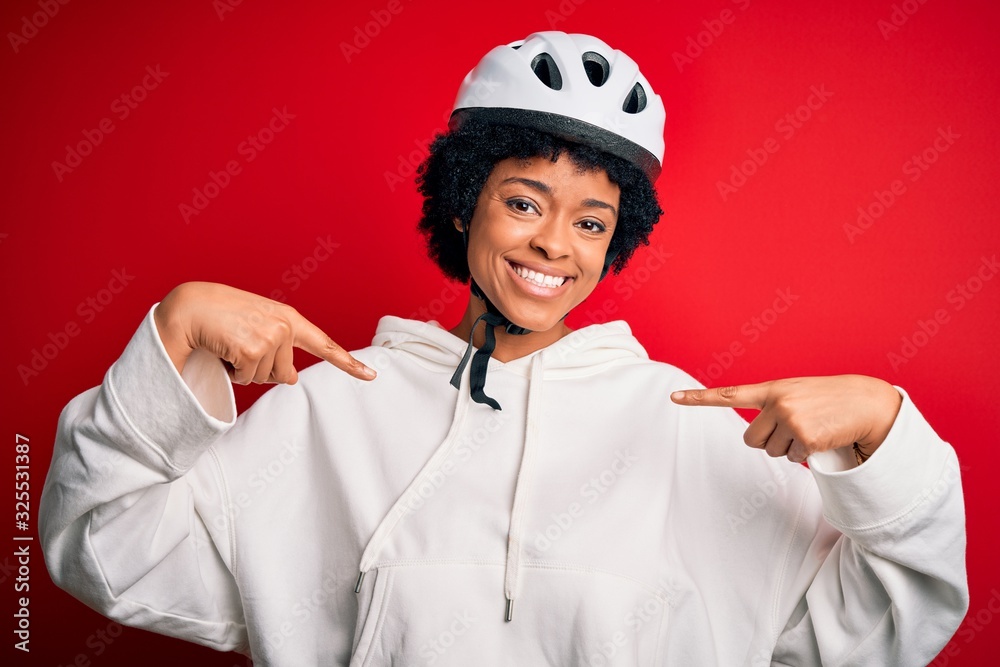 Young African American afro cyciling woman with curly hair wearing bike security helmet looking confident with smile on face, pointing oneself with fingers proud and happy. Young African American afro cyciling woman with curly hair wearing bike security helmet looking confident with smile on face, pointing oneself with fingers proud and happy.
