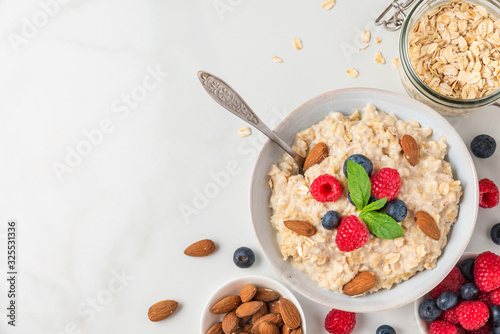 Bowl of oatmeal porridge with fresh berries, almonds and mint with a spoon for healthy diet breakfast on white table