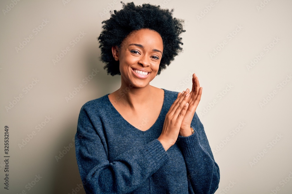 Young beautiful African American afro woman with curly hair wearing casual sweater clapping and applauding happy and joyful, smiling proud hands together Young beautiful African American afro woman with curly hair wearing casual sweater clapping and applauding happy and joyful, smiling proud hands together