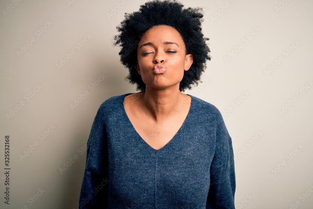 Young beautiful African American afro woman with curly hair wearing casual sweater looking at the camera blowing a kiss on air being lovely and sexy. Love expression. Young beautiful African American afro woman with curly hair wearing casual sweater looking at the camera blowing a kiss on air being lovely and sexy. Love expression.