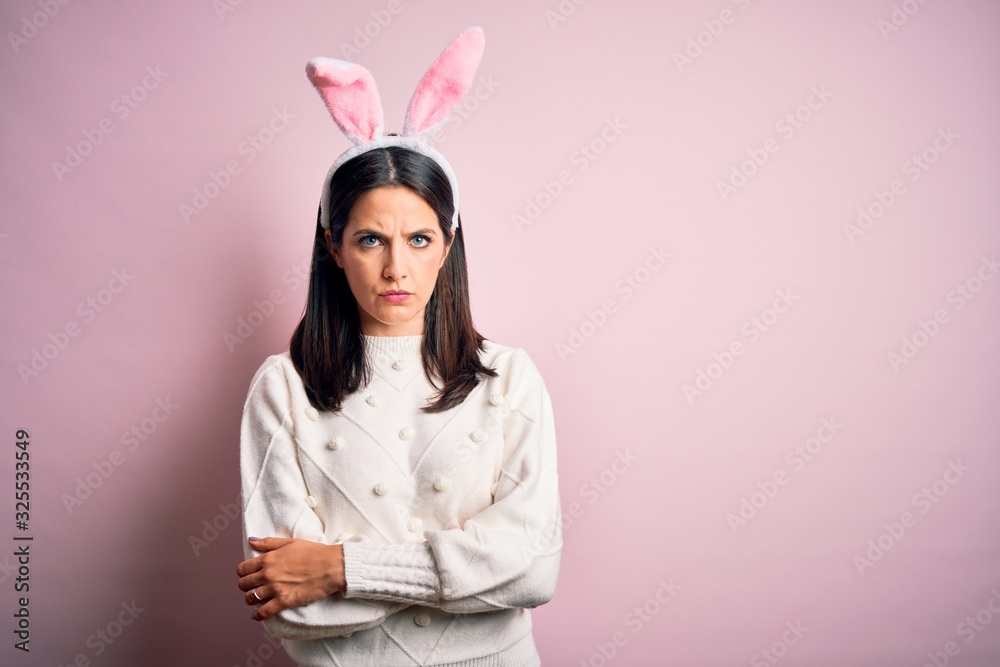 Young caucasian woman wearing cute easter rabbit ears over pink isolated background skeptic and nervous, disapproving expression on face with crossed arms. Negative person.