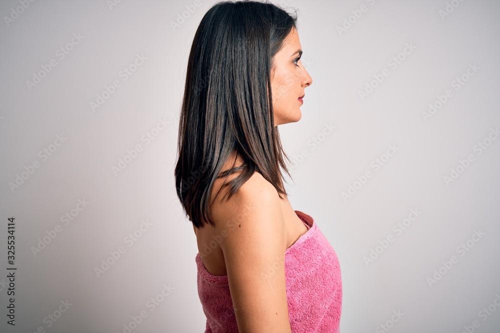 Young brunette woman with blue eyes wearing shower towel after bath over white background looking to side, relax profile pose with natural face with confident smile. Young brunette woman with blue eyes wearing shower towel after bath over white background looking to side, relax profile pose with natural face with confident smile.