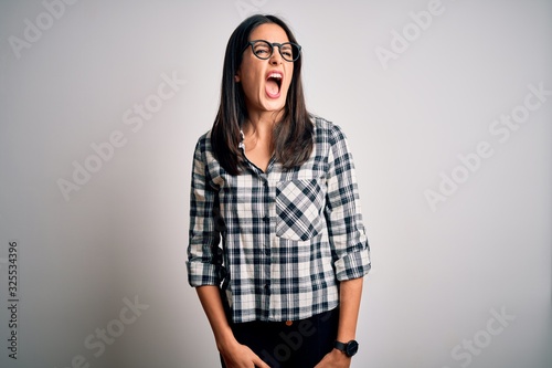 Young brunette woman with blue eyes wearing casual shirt and glasses over white background angry and mad screaming frustrated and furious, shouting with anger. Rage and aggressive concept. © Krakenimages.com