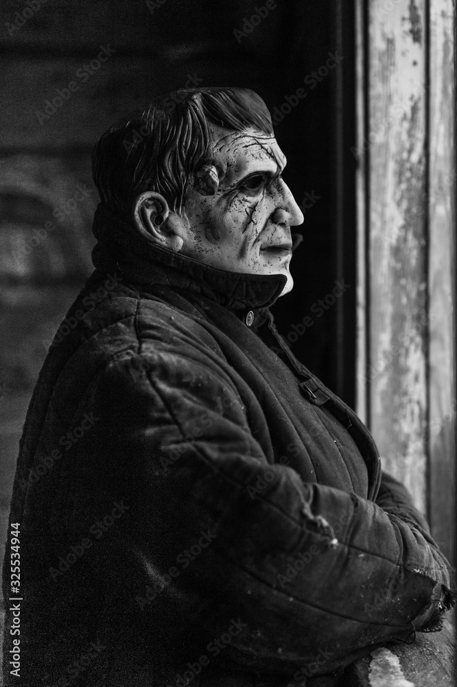 Frightening man in a terrible monster mask peeks out an old dirty window in village