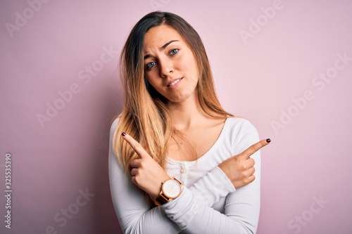 Young beautiful blonde woman with blue eyes wearing white t-shirt over pink background Pointing to both sides with fingers  different direction disagree