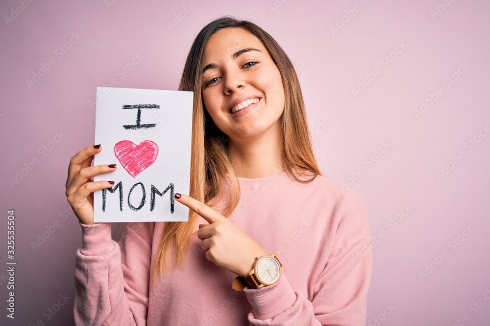 Young beautiful woman holding paper with love mom message celebrating mothers day very happy pointing with hand and finger Young beautiful woman holding paper with love mom message celebrating mothers day very happy pointing with hand and finger