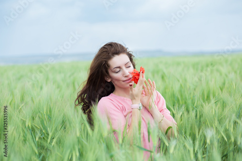 Outdoor portrait of a beautiful woman smelling poppy flowers in a wheat field