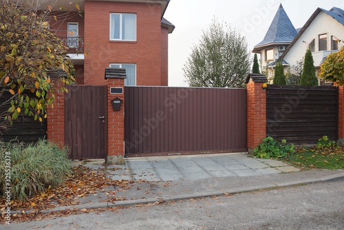 one brown iron gate and a fence of bricks and wooden boards on the street