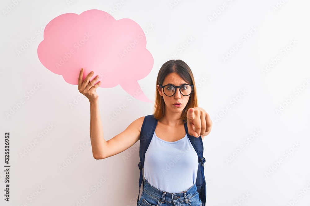 Beautiful redhead student woman wearing a backpack and holding speech bubble pointing with finger to the camera and to you, hand sign, positive and confident gesture from the front Beautiful redhead student woman wearing a backpack and holding speech bubble pointing with finger to the camera and to you, hand sign, positive and confident gesture from the front
