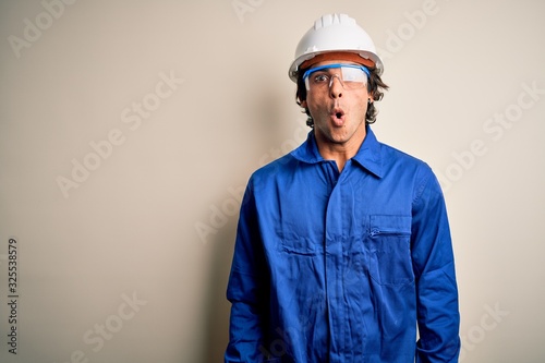 Young constructor man wearing uniform and security helmet over isolated white background afraid and shocked with surprise expression, fear and excited face.