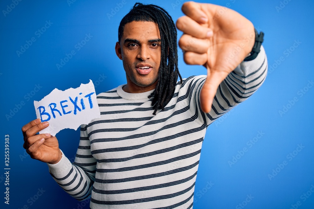Fototapeta premium Young african american afro man holding banner with brexit message over blue background with angry face, negative sign showing dislike with thumbs down, rejection concept