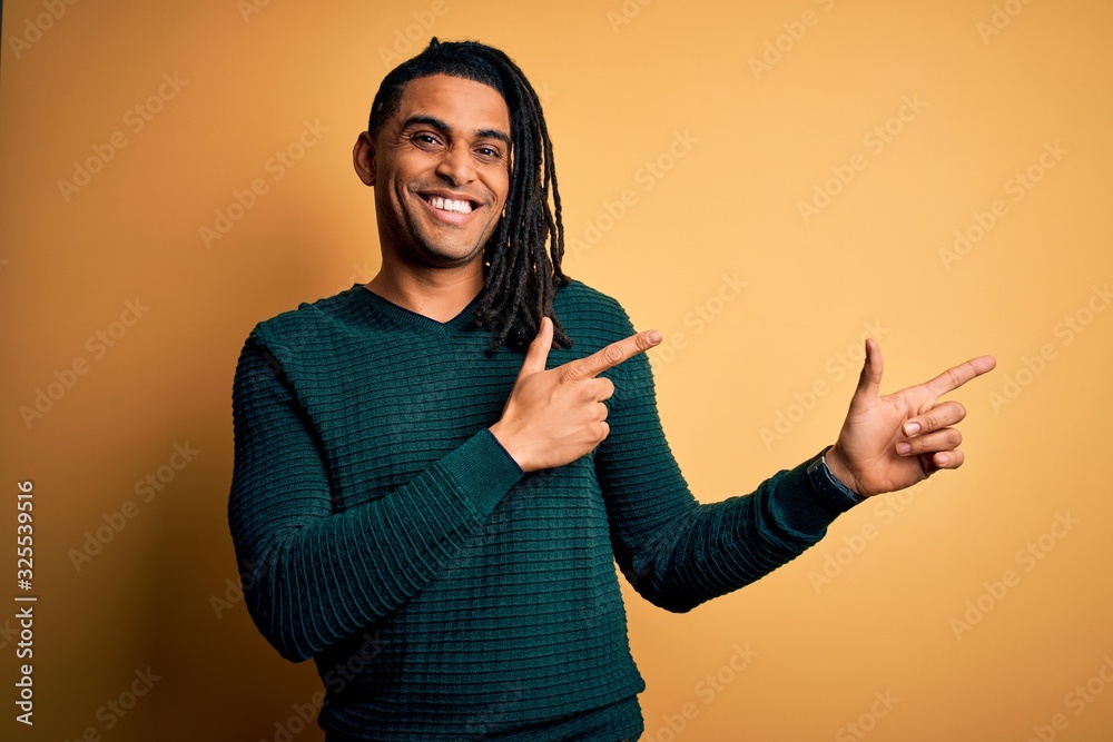Young handsome african american afro man with dreadlocks wearing green casual sweater smiling and looking at the camera pointing with two hands and fingers to the side. Young handsome african american afro man with dreadlocks wearing green casual sweater smiling and looking at the camera pointing with two hands and fingers to the side.