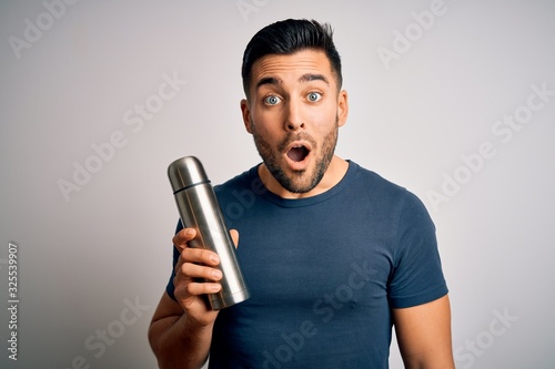 Young handsome tourist man drinking thermo with water over isolated white background scared in shock with a surprise face, afraid and excited with fear expression