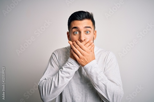 Young handsome man wearing casual t-shirt standing over isolated white background shocked covering mouth with hands for mistake. Secret concept.