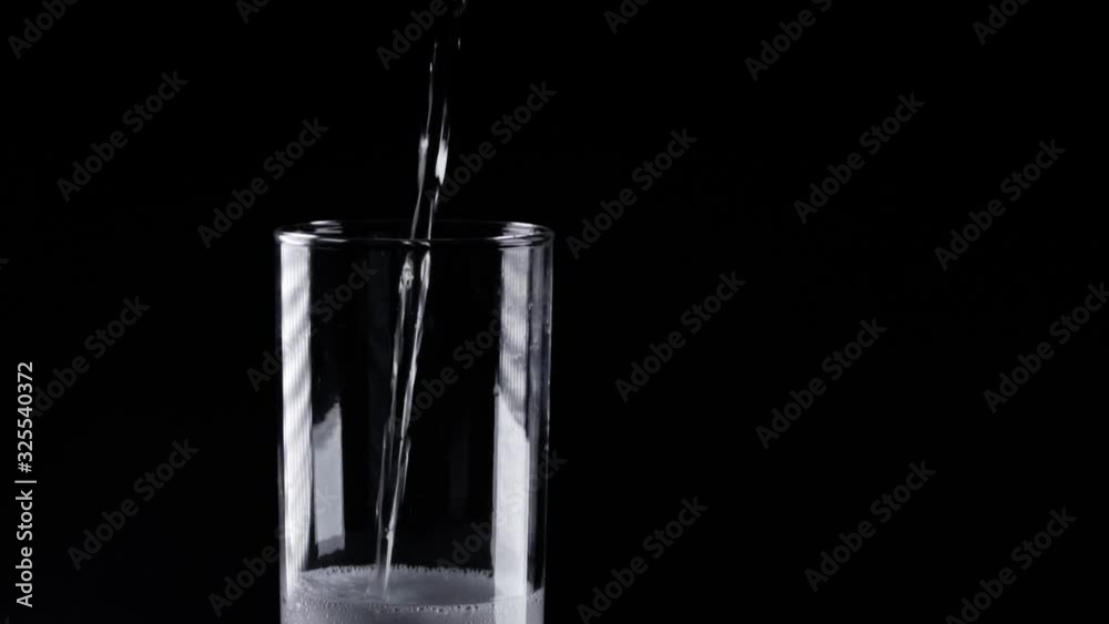 transparent soda poured into tall glass in super slow motion against a black background transparent soda poured into tall glass in super slow motion against a black background