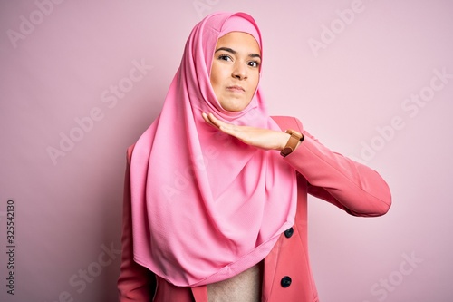 Young beautiful girl wearing muslim hijab standing over isolated pink background cutting throat with hand as knife, threaten aggression with furious violence © Krakenimages.com