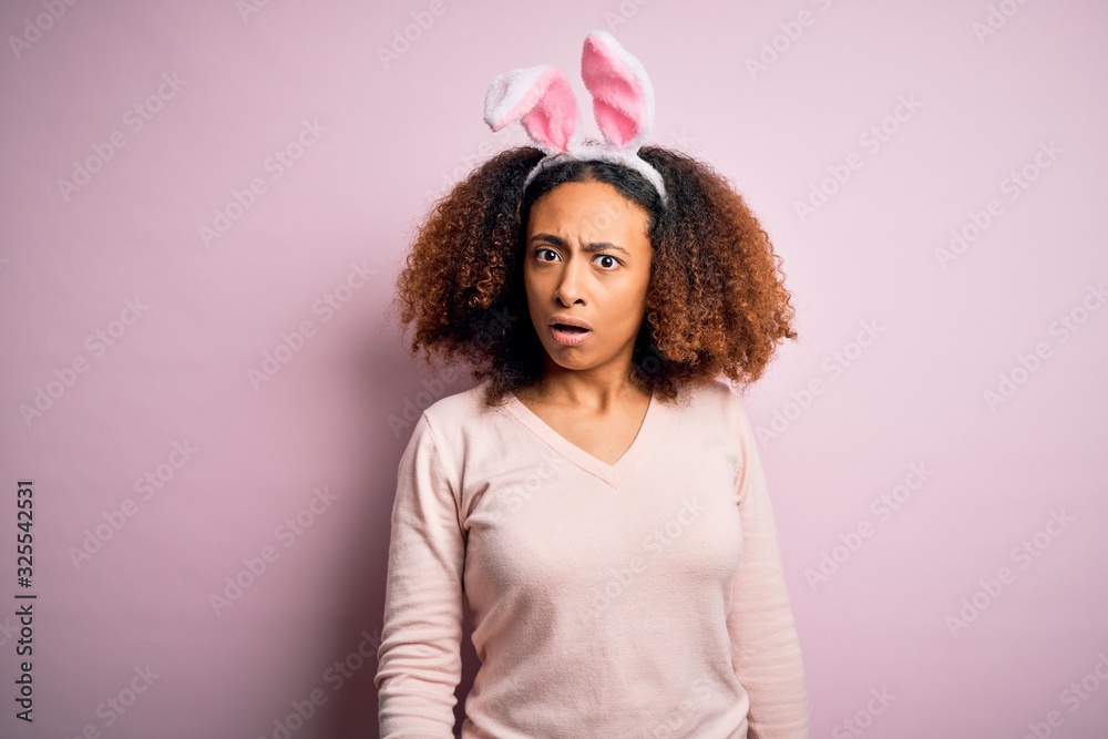 Young african american woman with afro hair wearing bunny ears over pink background In shock face, looking skeptical and sarcastic, surprised with open mouth Young african american woman with afro hair wearing bunny ears over pink background In shock face, looking skeptical and sarcastic, surprised with open mouth