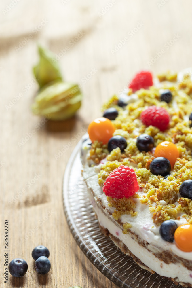 Moostorte aus grünem Biscuit mit Quark, Sahne, Früchte, Blaubeere, Himbeere, Physalis auf Holz Moostorte aus grünem Biscuit mit Quark, Sahne, Früchte, Blaubeere, Himbeere, Physalis auf Holz