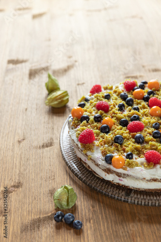 Moostorte aus grünem Biscuit mit Quark, Sahne, Früchte, Blaubeere, Himbeere, Physalis auf Holz