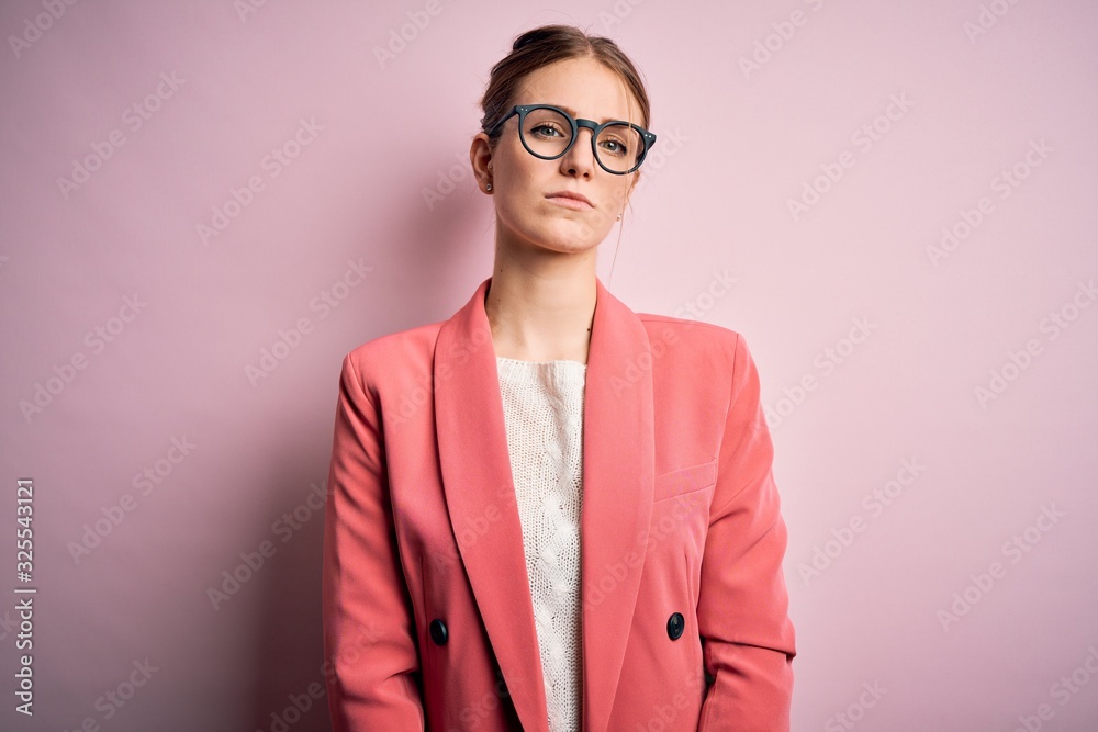 Young beautiful redhead woman wearing jacket and glasses over isolated pink background Relaxed with serious expression on face. Simple and natural looking at the camera.