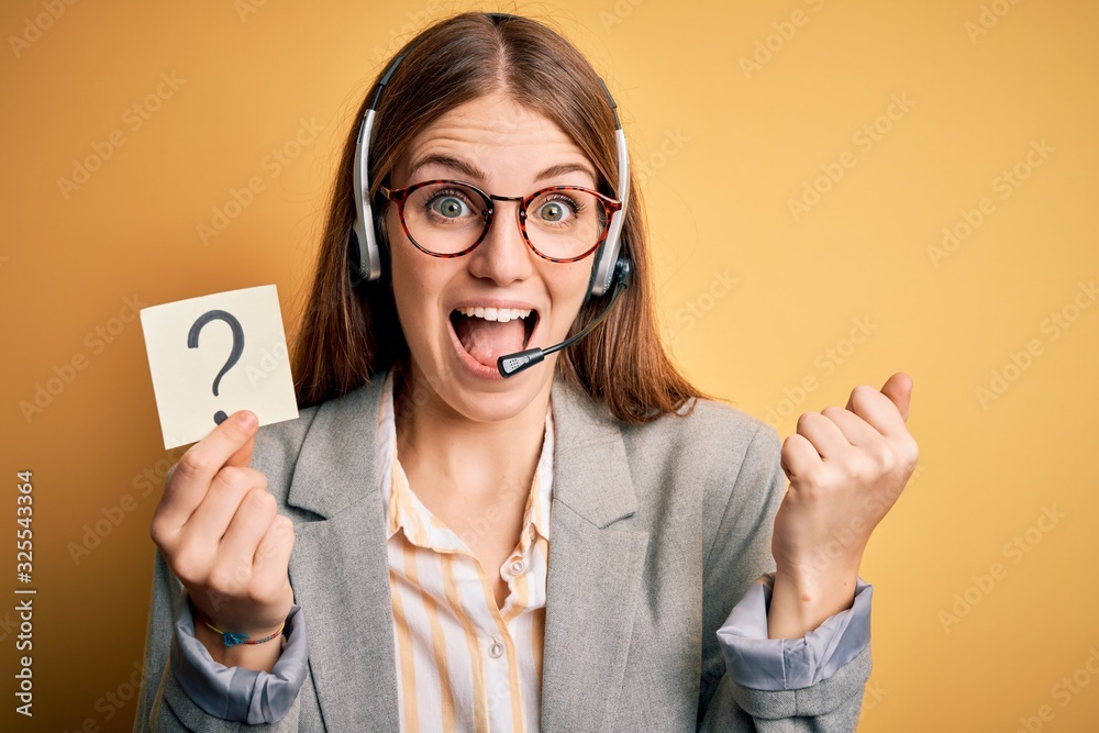 Young redhead call center agent woman using headset holding question mark reminder screaming proud and celebrating victory and success very excited, cheering emotion Young redhead call center agent woman using headset holding question mark reminder screaming proud and celebrating victory and success very excited, cheering emotion
