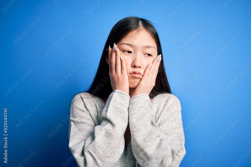 Young beautiful asian woman wearing casual sweater standing over blue isolated background Tired hands covering face, depression and sadness, upset and irritated for problem Young beautiful asian woman wearing casual sweater standing over blue isolated background Tired hands covering face, depression and sadness, upset and irritated for problem