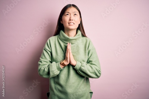 Young beautiful asian woman wearing green winter sweater over pink solated background begging and praying with hands together with hope expression on face very emotional and worried. Begging. © Krakenimages.com