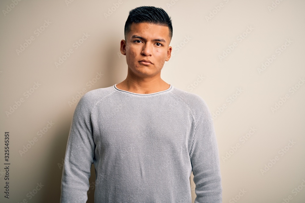 Young handsome latin man wearing casual sweater standing over isolated white background Relaxed with serious expression on face. Simple and natural looking at the camera. Young handsome latin man wearing casual sweater standing over isolated white background Relaxed with serious expression on face. Simple and natural looking at the camera.
