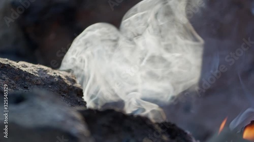 Smoke is rising from a smoldering campfire surrounded by rocks