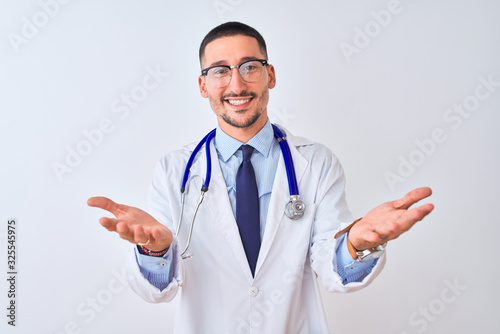 Young doctor man wearing stethoscope over isolated background smiling cheerful offering hands giving assistance and acceptance.