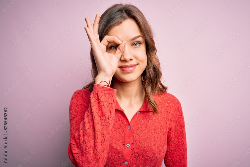 Young beautiful blonde casual girl over pink isolated background doing ok gesture with hand smiling, eye looking through fingers with happy face. Young beautiful blonde casual girl over pink isolated background doing ok gesture with hand smiling, eye looking through fingers with happy face.