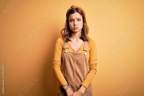 Young beautiful blonde girl wearing overall standing over yellow isolated background depressed and worry for distress, crying angry and afraid. Sad expression.