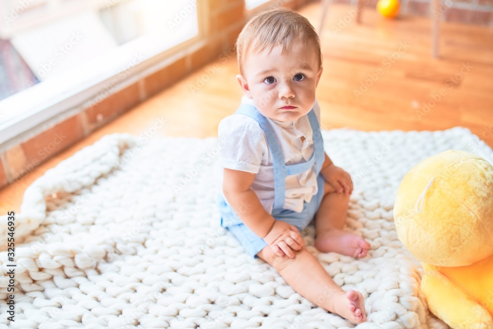 Fototapeta premium Beautiful toddler sitting on the blanket playing with duck doll at kindergarten