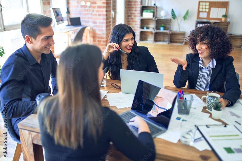 Group of business workers smiling happy and confident. Working together with smile on face using laptop and speaking at the office Group of business workers smiling happy and confident. Working together with smile on face using laptop and speaking at the office