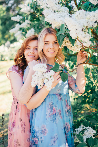 Beautiful sisters with blonde and brown hair in a lilac garden spend time together and smile
