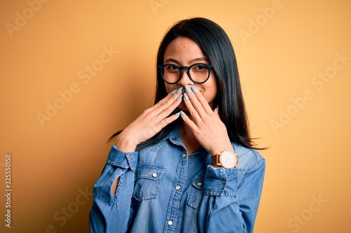 Foto Young beautiful chinese woman wearing casual denim shirt over isolated yellow ba