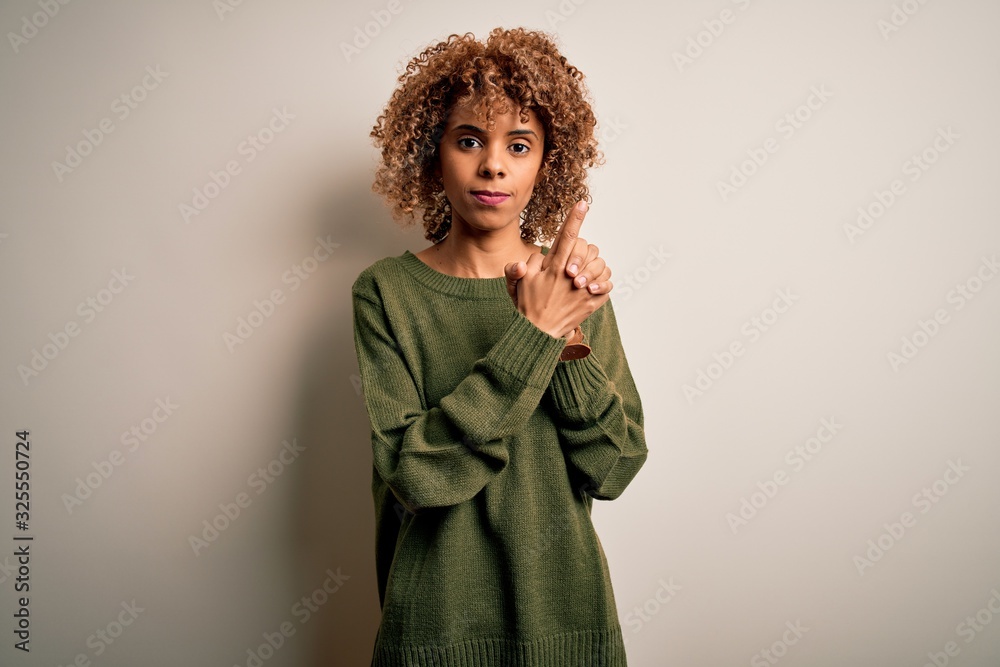 Beautiful african american woman with curly hair wearing casual sweater over white background Holding symbolic gun with hand gesture, playing killing shooting weapons, angry face Beautiful african american woman with curly hair wearing casual sweater over white background Holding symbolic gun with hand gesture, playing killing shooting weapons, angry face