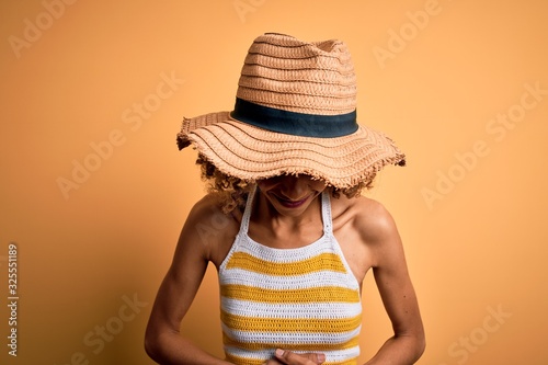 African american tourist woman with curly on vacation wearing summer hat and striped t-shirt with hand on stomach because indigestion, painful illness feeling unwell. Ache concept.