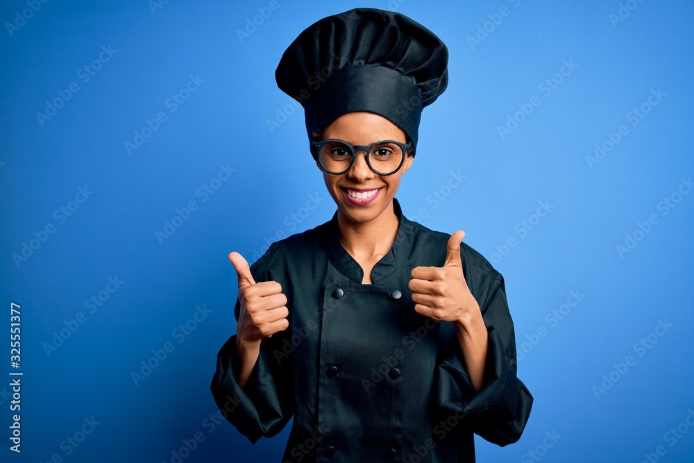 Young african american chef woman wearing cooker uniform and hat over blue background success sign doing positive gesture with hand, thumbs up smiling and happy. Cheerful expression and winner Young african american chef woman wearing cooker uniform and hat over blue background success sign doing positive gesture with hand, thumbs up smiling and happy. Cheerful expression and winner