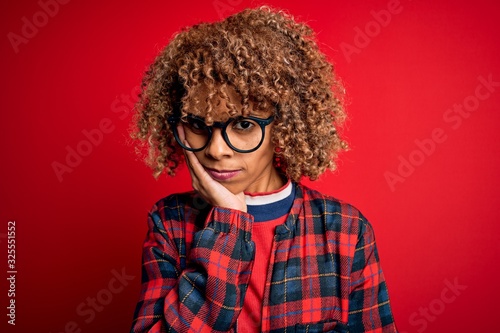 Young beautiful african american woman wearing casual shirt and glasses over red background thinking looking tired and bored with depression problems with crossed arms. © Krakenimages.com