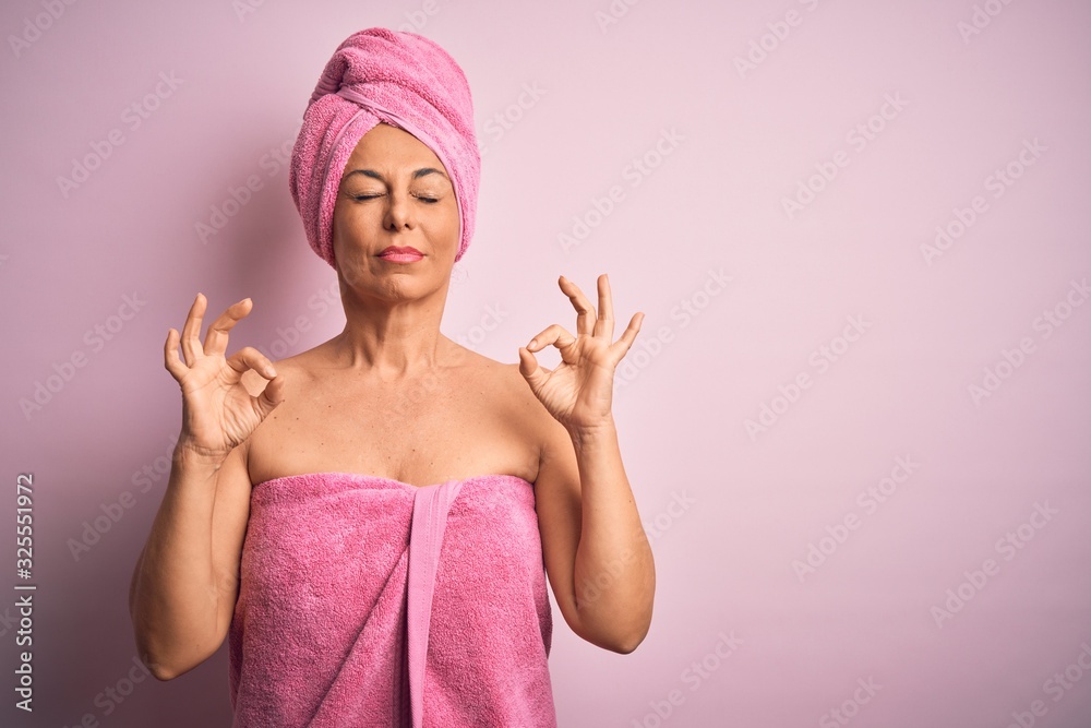 Middle age woman wearing bath towel from beauty body care over pink background relax and smiling with eyes closed doing meditation gesture with fingers. Yoga concept. Middle age woman wearing bath towel from beauty body care over pink background relax and smiling with eyes closed doing meditation gesture with fingers. Yoga concept.