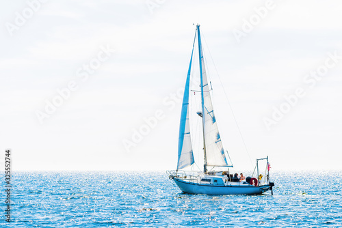 White sloop rigged yacht sailing in a Mediterranean sea on a clear sunny day, Spain. Blue sky with white clouds, reflections on water; photo