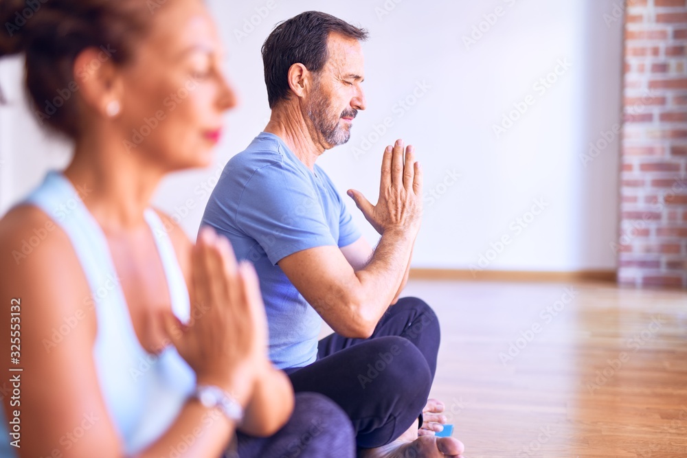 Middle age beautiful sporty couple sitting on mat practicing yoga doing prayer pose at gym Middle age beautiful sporty couple sitting on mat practicing yoga doing prayer pose at gym