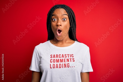 Young african american woman wearing sarcasm coments text on t-shirt over red background scared in shock with a surprise face, afraid and excited with fear expression photo