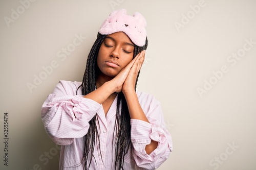 Young african american woman wearing pink pajama and sleep mask over isolated background sleeping tired dreaming and posing with hands together while smiling with closed eyes.