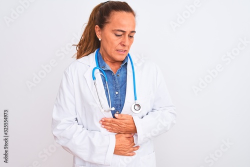 Middle age mature doctor woman wearing stethoscope over isolated background with hand on stomach because nausea, painful disease feeling unwell. Ache concept.
