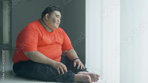 Obese man daydreaming somberly near the window photo