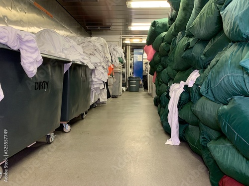 Laundry crew are working on the cruise ship. Huge operation on a luxury vessel. White trolley. Staff is wearing a professional uniform.