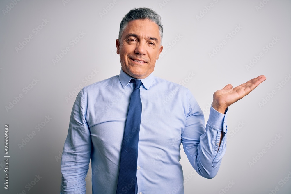 Middle age handsome grey-haired business man wearing elegant shirt and tie smiling cheerful presenting and pointing with palm of hand looking at the camera. Middle age handsome grey-haired business man wearing elegant shirt and tie smiling cheerful presenting and pointing with palm of hand looking at the camera.
